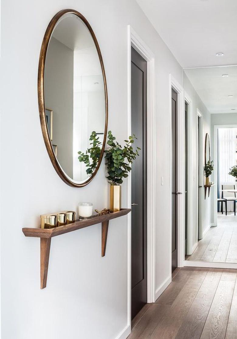 round mirror in hallway above wall-mounted shelf