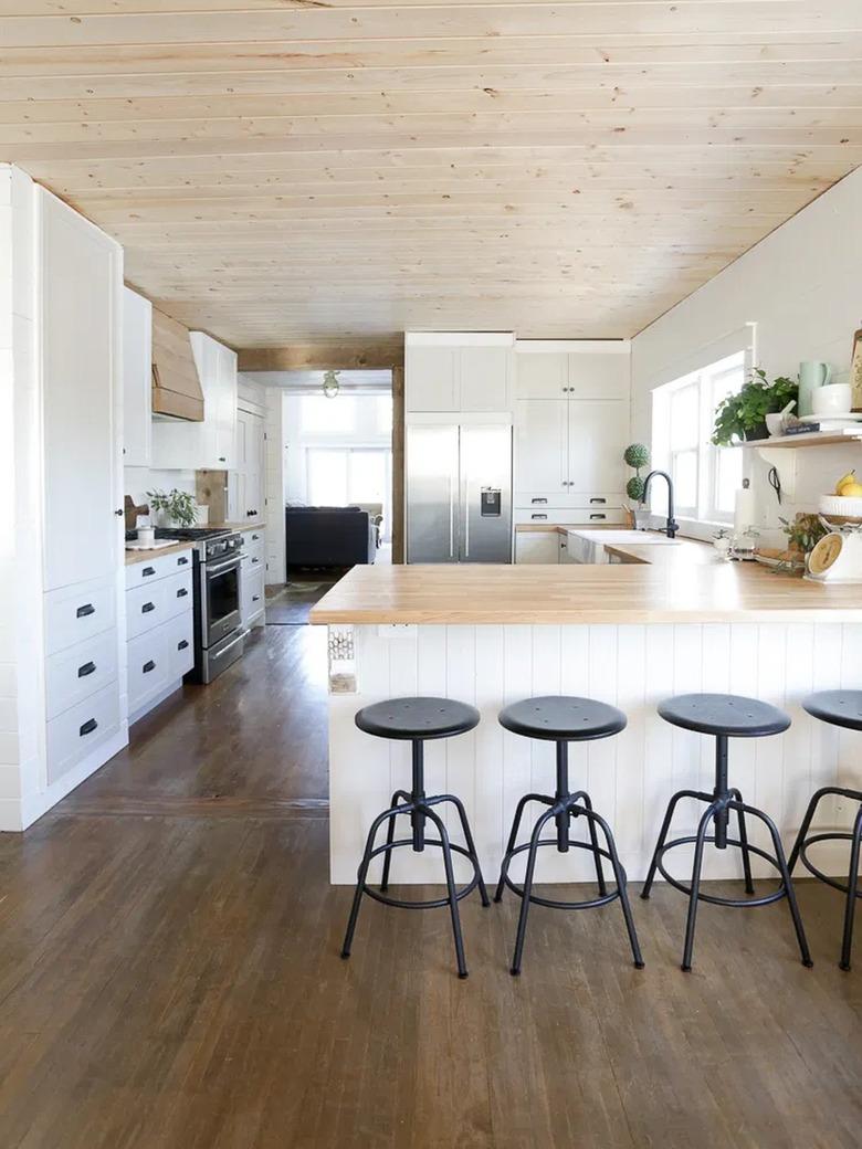 white and wood l-shaped kitchen with black bar stools