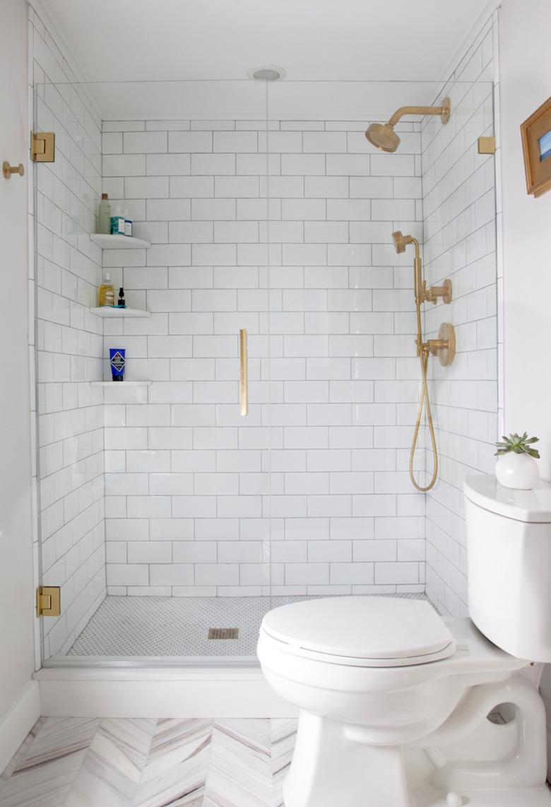 Photo of white tiled bathroom with glass walk-in shower.