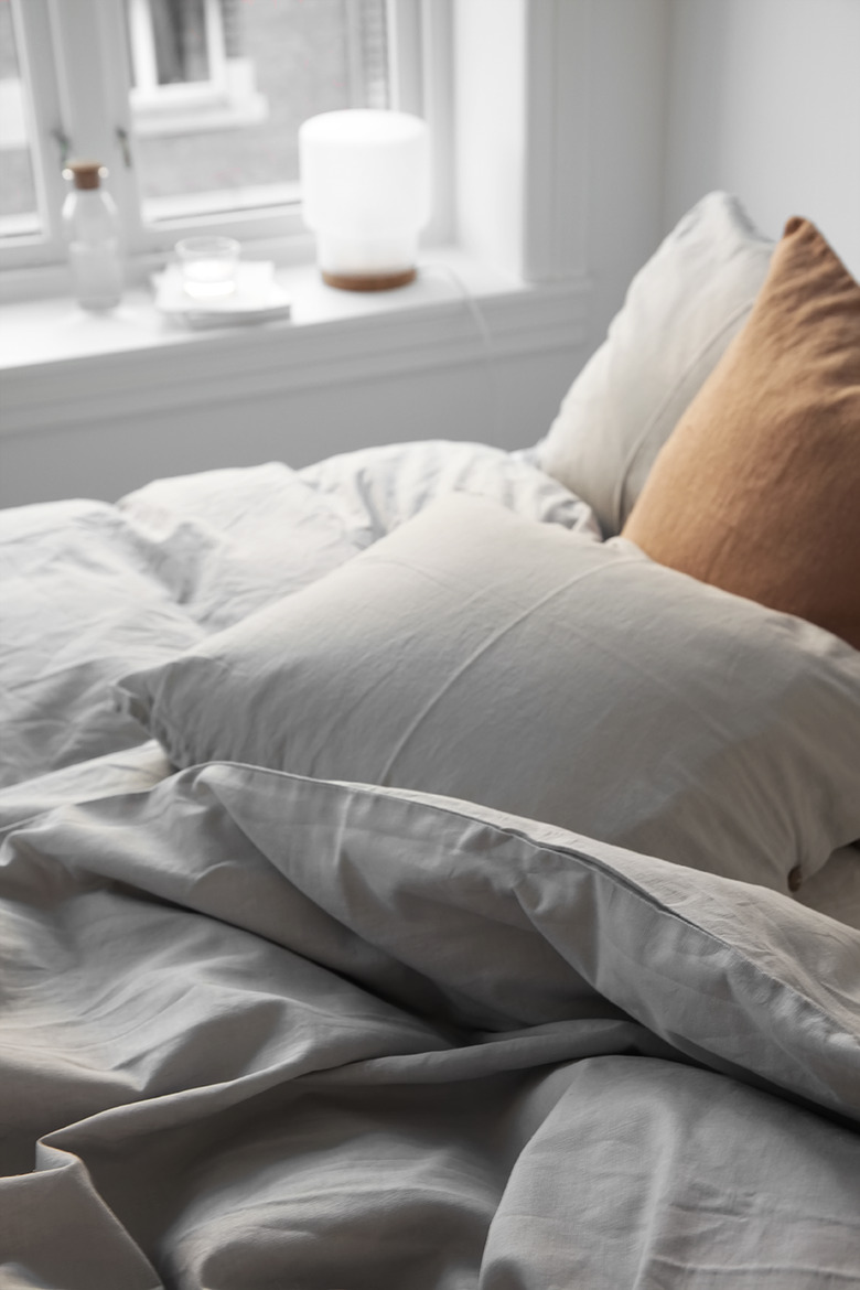 A wrinkled white duvet and a tan pillow.