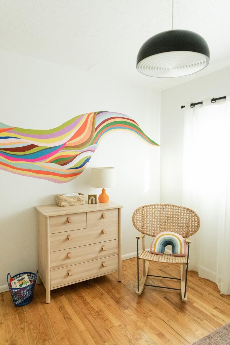 Nursery with wood floors and dresser, black bowl pendant light and colorful wall mural