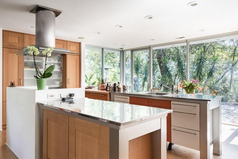 Modern kitchen with wood cabinets, steel counters, long car handles, and full-glass windows.