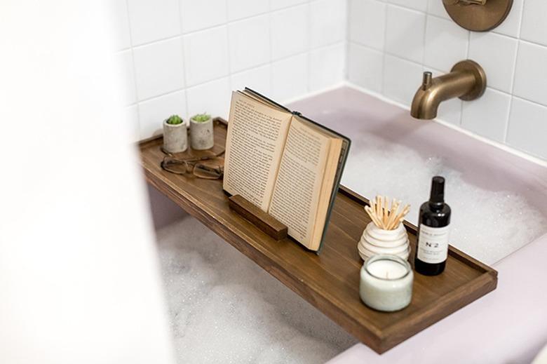 Wood bath tray with reading glasses, book, and plants over bathtub