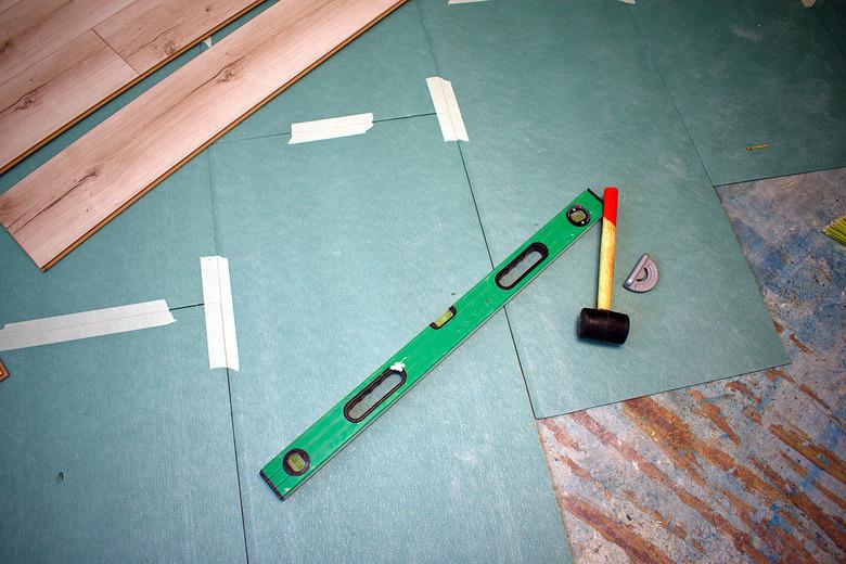 Underlayment for laminate and laminate flooring. Nearby there is a level, a mallet and a corner.