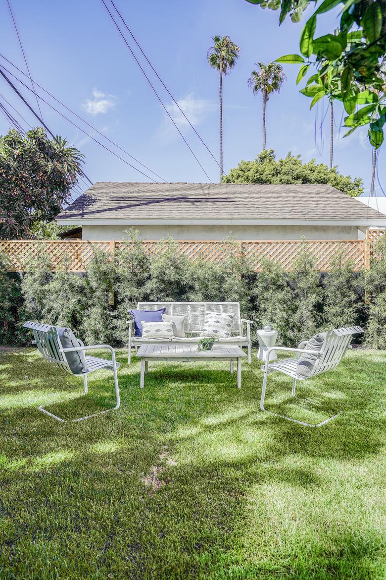 a lush green lawn with white patio furniture; palm trees are in the background