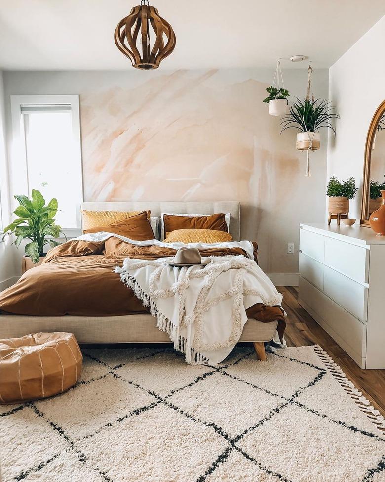 Boho bedroom with blush accent wall and hanging plants.