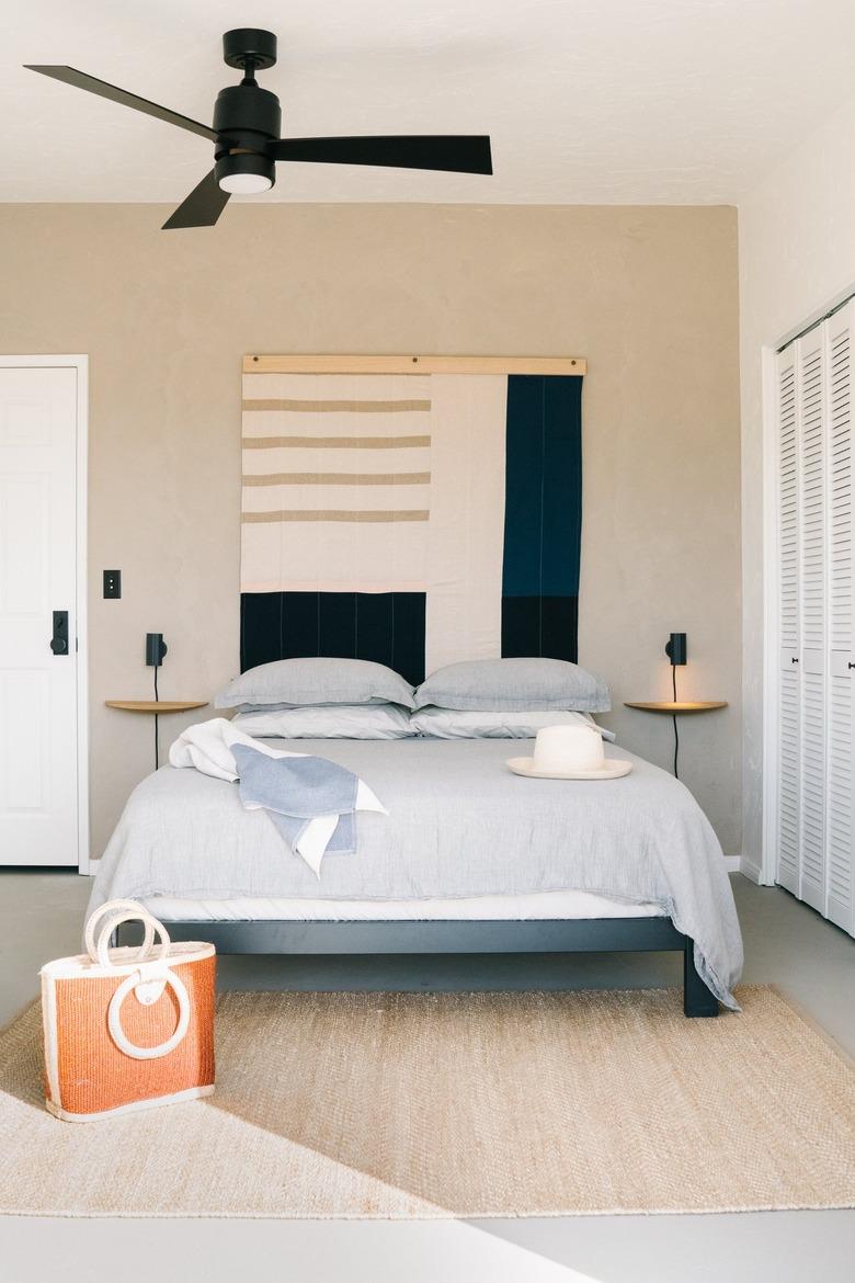 beige accent wall with tapestry hanging behind bed