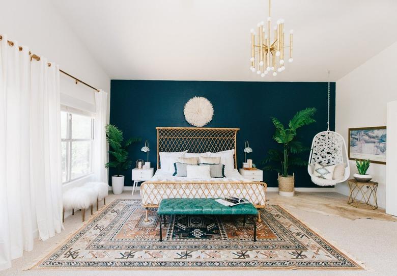 Bright bedroom with dark blue accent wall, white curtains and a boho hanging chair.