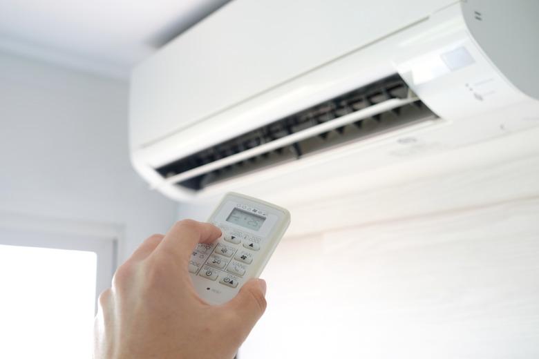 Man's hand using remote control open The air conditioner is cooled to 25 degrees Celsius in his bedroom. Health concepts and energy savings