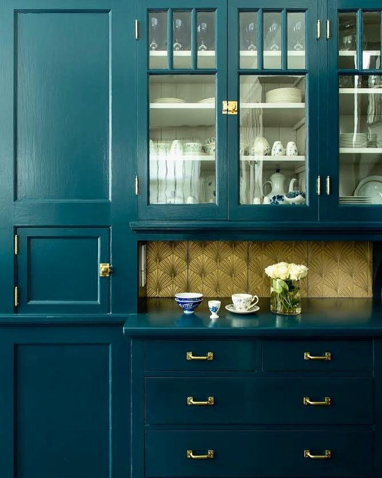 Gold art deco backsplash with leaf design alongside teal cabinets