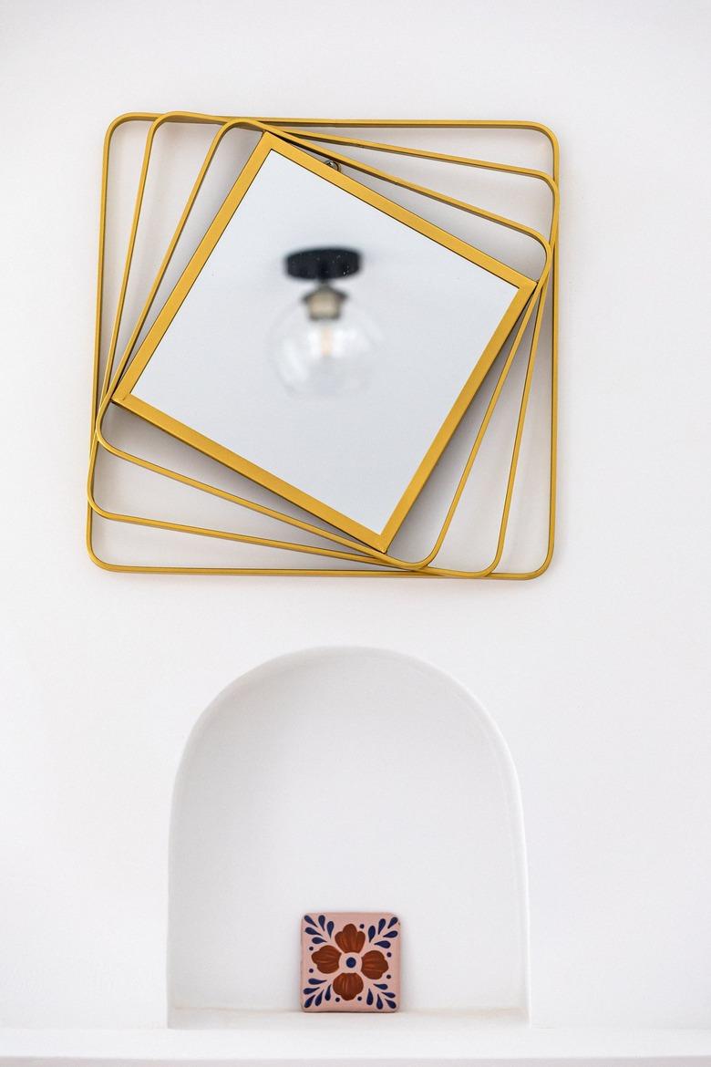 An abstract yellow mirror over a white wall niche with a red flower tile