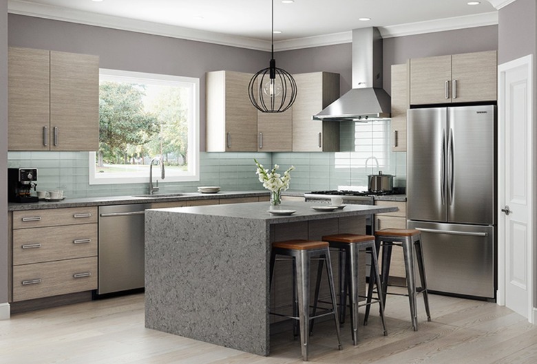 Kitchen with bamboo cabinets, waterfall island, barstools, pendant lamp, stainless appliances.