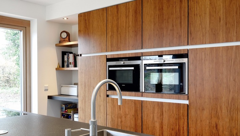 kitchen with bamboo cabinets, ovens in wall, open shelves.