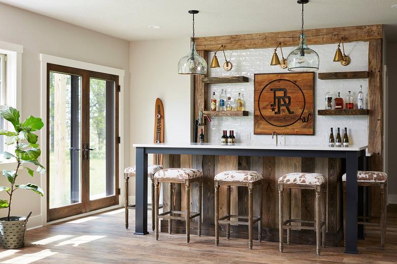 rustic basement bar with subway tile backsplash and cowhide stools