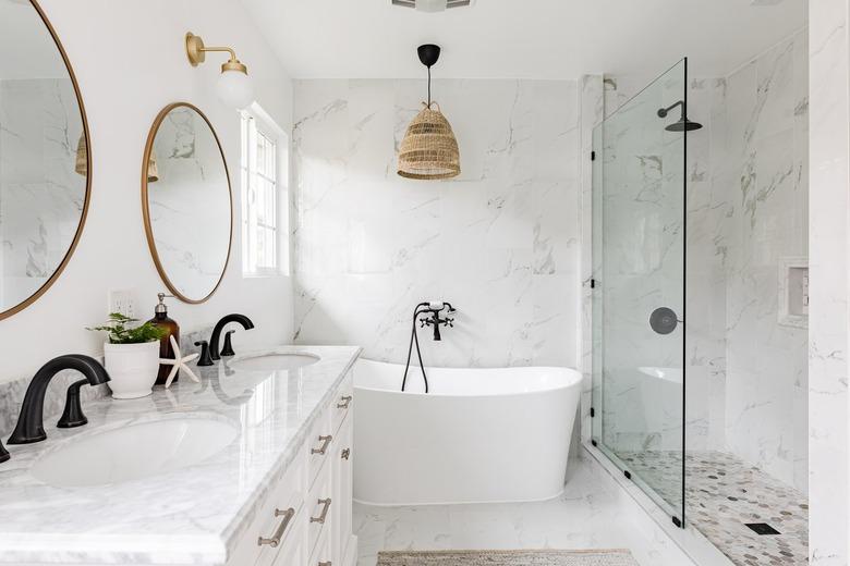 Minimalist white bathroom with a glass shower, bathtub and large round mirrors