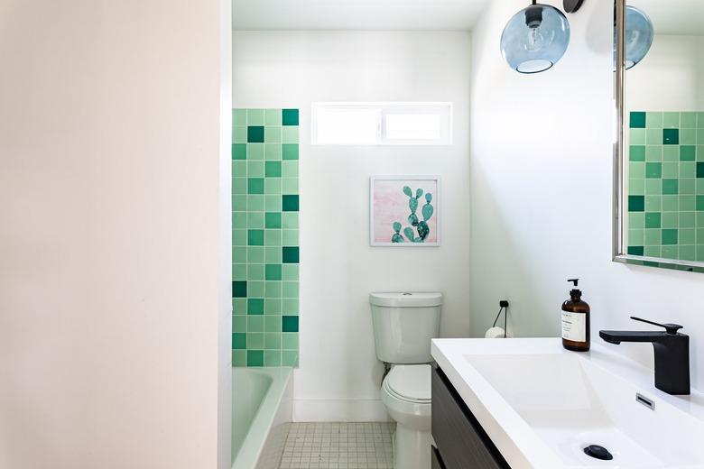 A small bathroom with green tile, a small sink with a black single faucet