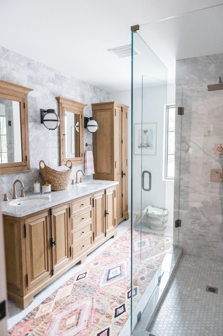 Bathroom rug idea with bohemian flair paired with wood cabinets and glass shower enclosure