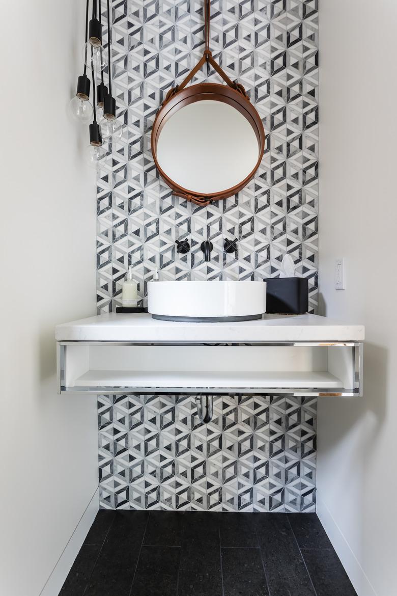 Bathroom under stairs with gray and white modern backsplash and round mirror