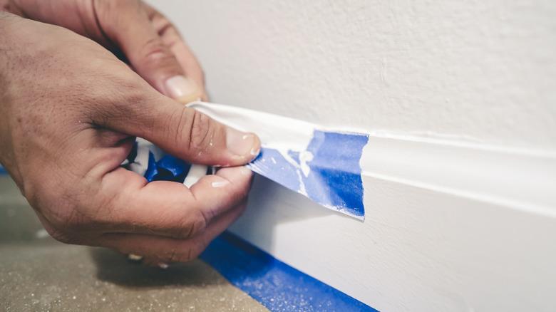 Removing masking tape from moulding. A painter pulls of blue painter's tape from the wall to reveal a clean edge baseboard.