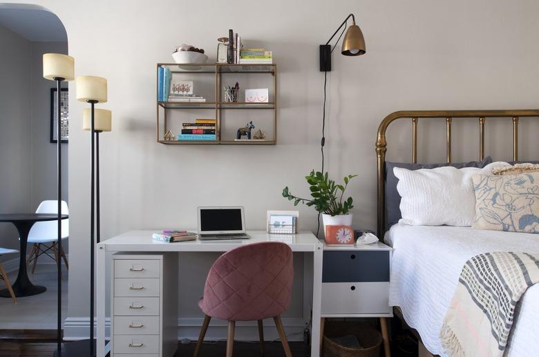 A bedroom with an office desk and a pink velvet chair