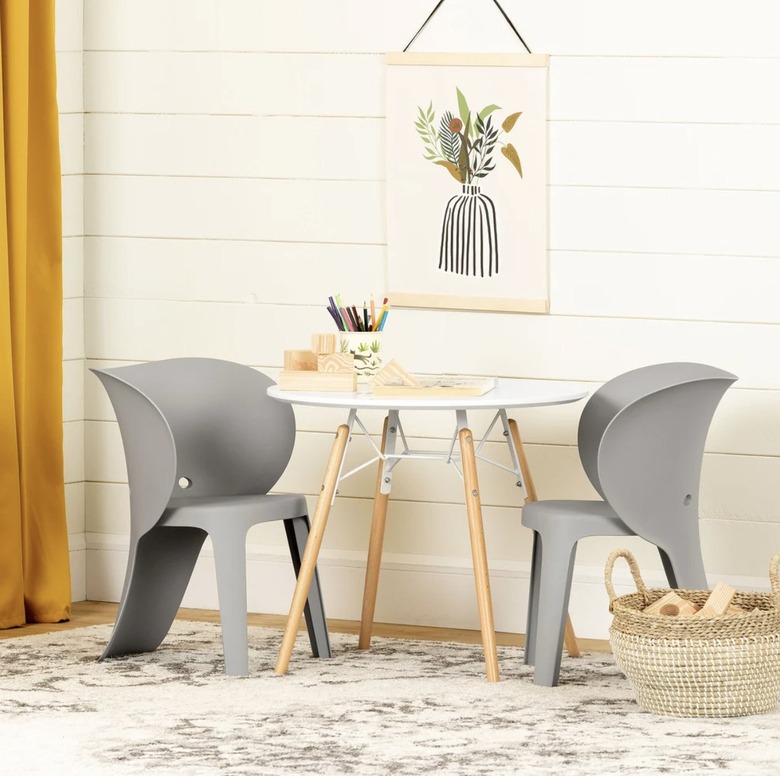 Kids' table and chairs shaped like elephant trunks in a playroom with white wall and an area rug