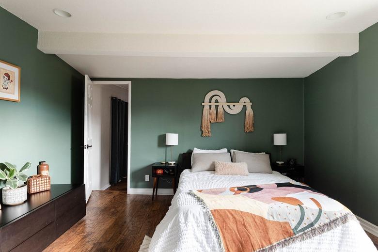 A green-walled bedroom with wood floors and neutral-beige accents