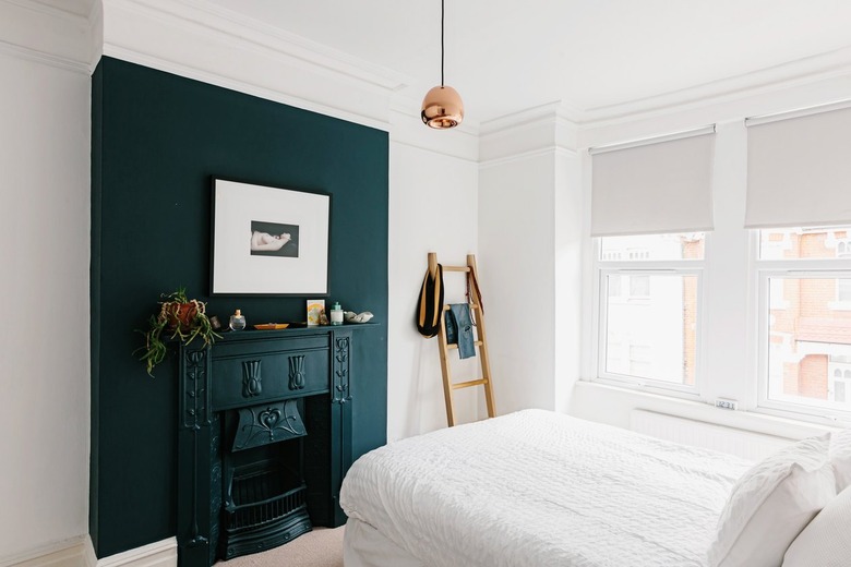 Dark turquoise mantle against white wall in small bedroom with windows and ladder propped against wall