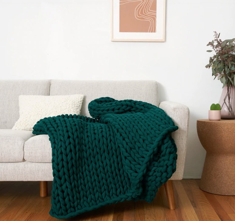 Weighted blanket resting on couch, end table, plant, art.