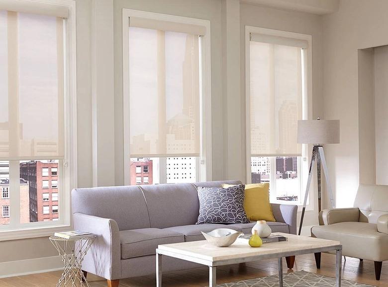 A living room with three windows that are covered in neutral colored solar shades