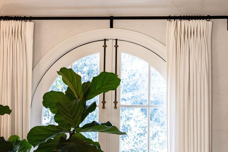 An arched window with white curtains and a tree plant