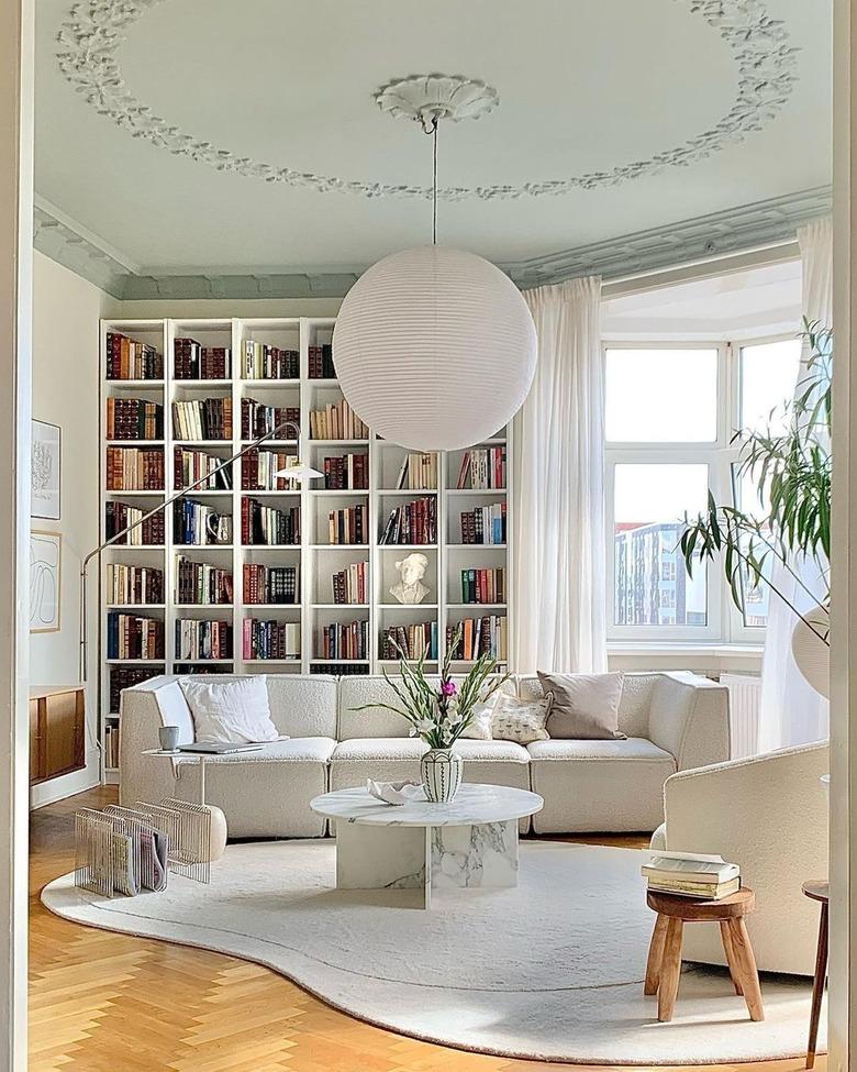 A white room with a white couch, white coffee table, and white bookshelf in the background.