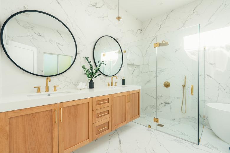 marble bathroom with pair of round mirrors and brass shower fixtures