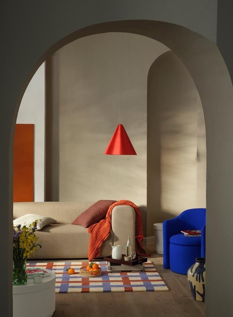 A red pendant lamp hanging in a beige living room with red and blue accents.