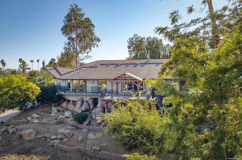 Exterior of a house in California that is built into rocks and partially covered by trees in front of a blue sky.