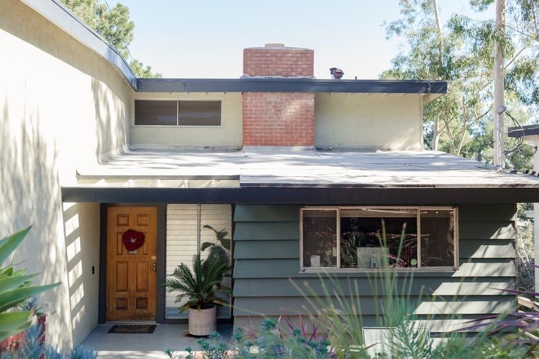 A midcentury modern house with a brick chimney, gray and white exterior, and wood door.