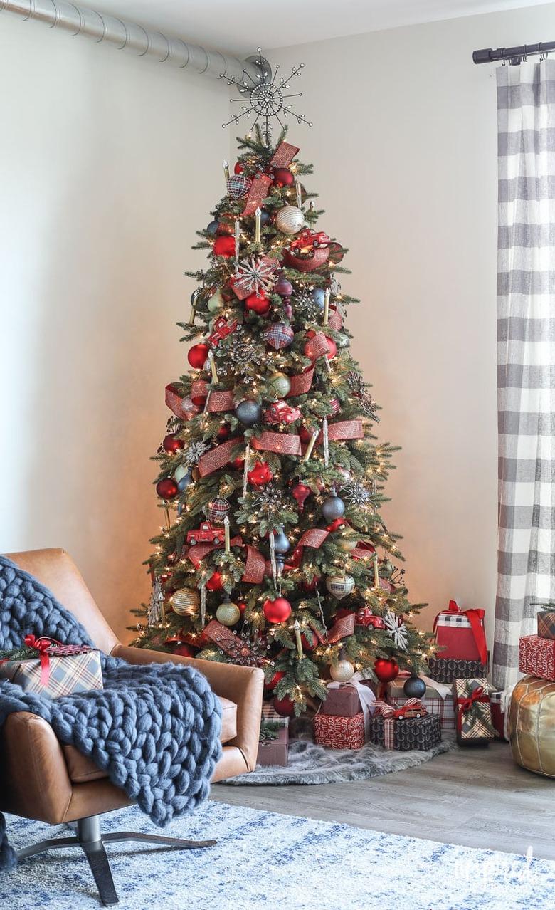 Christmas Tree Themes with Rustic style Christmas tree decorated with red and multi colored ornaments, leather lounge chair, gray and white checked curtain.