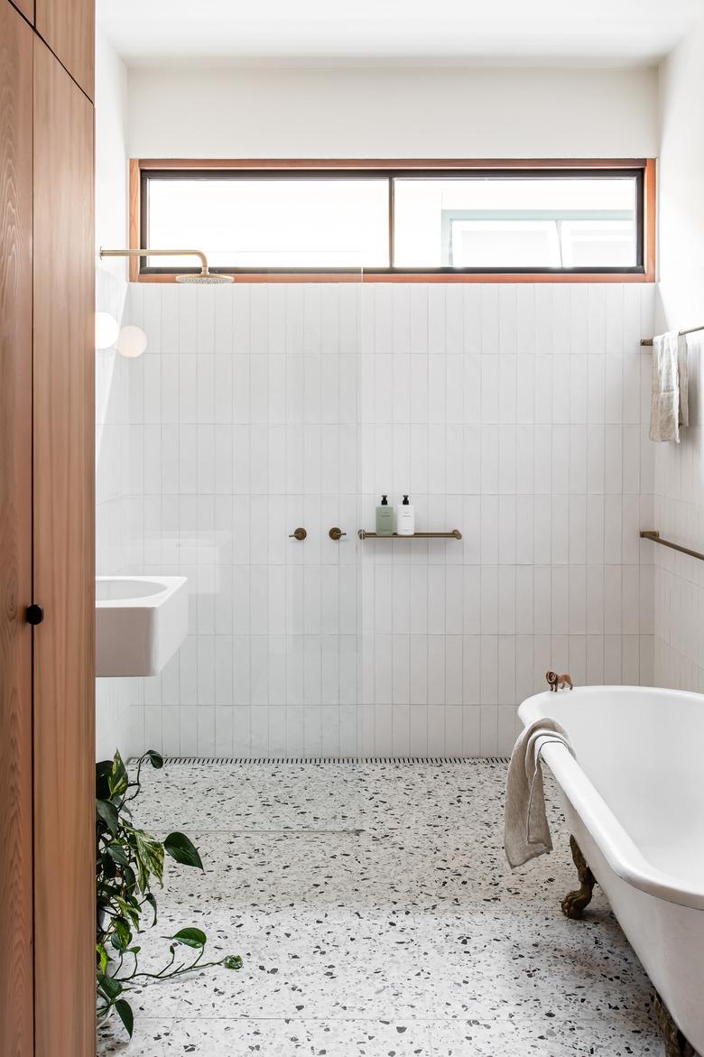 white modern bathroom with terrzzo floors and a clawfoot tub next to a standing shower