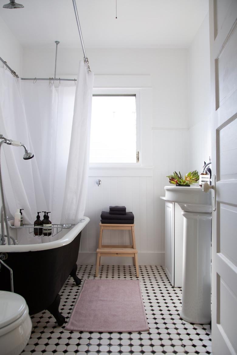 the walls, shower curtain, and most fixtures in this bathroom are white; the floor is black and white tile, and the tub stark black