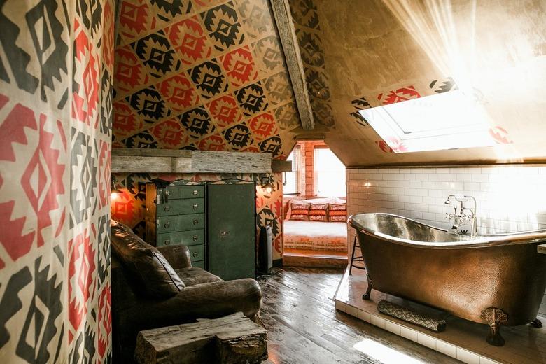 a bathroom with a distressed wood floor, a worn leather couch, and a metal claw-foot tub under a skylight