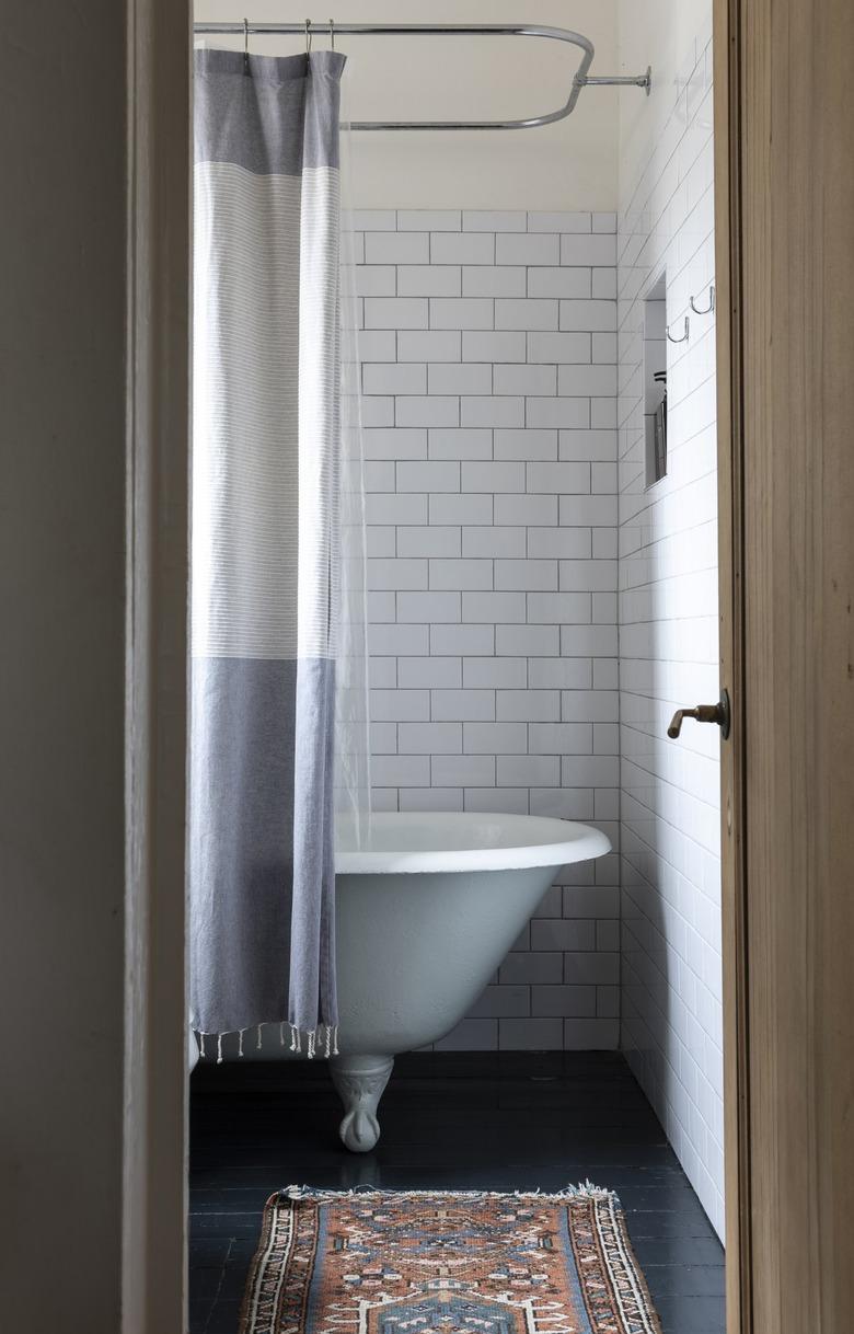 a bathroom with subway tile, a small throw rug, and a claw-foot tub with a gray and white curtain