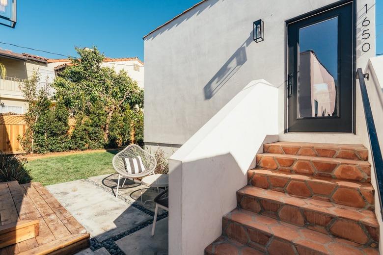 White house with terra-cotta tile roof and steps, outdoor furniture, and casement door