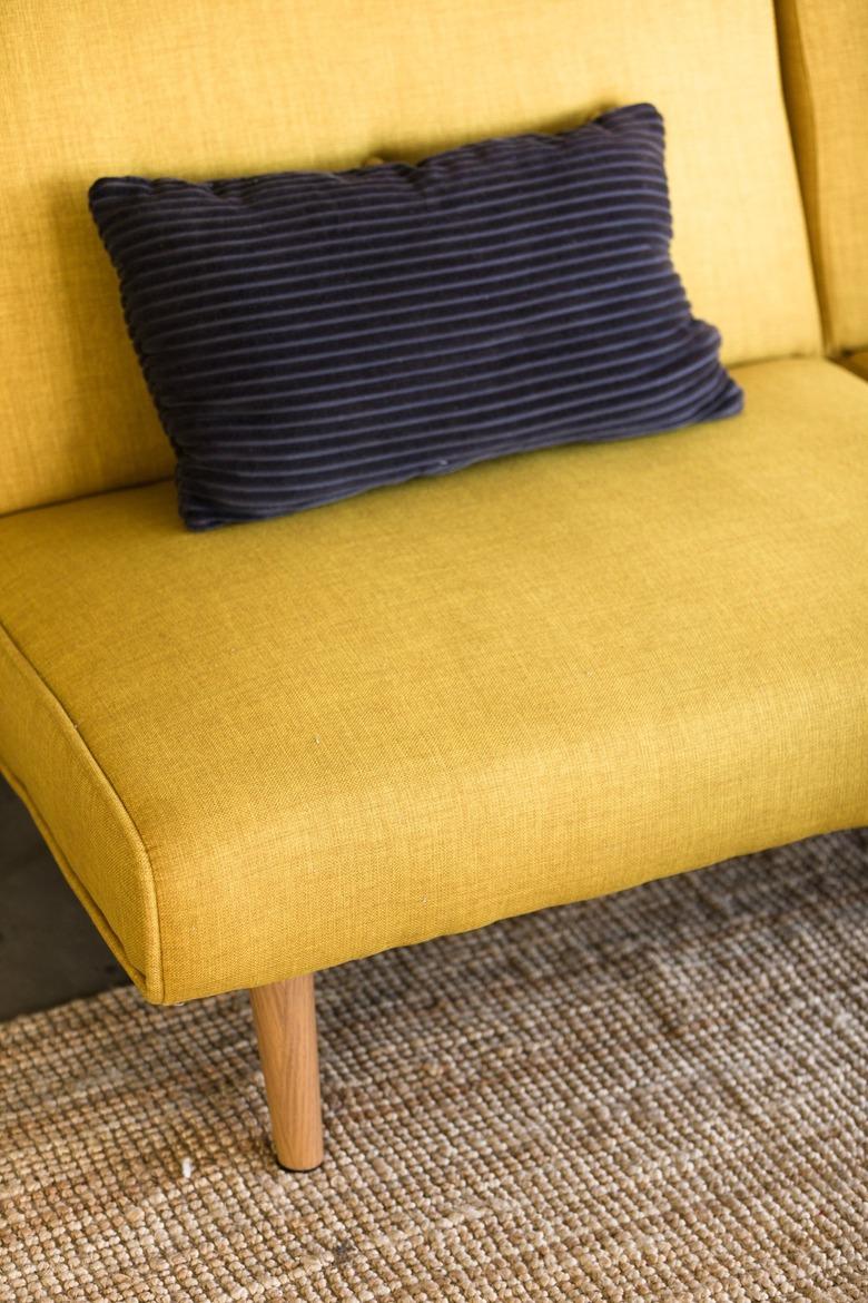 a mustard-yellow mid-century couch with a black throw pillow