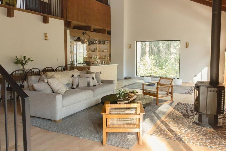 Living room with eclectic furniture, stove fireplace, stone hearth, and picture windows. A wood ceiling and wood wall accents.