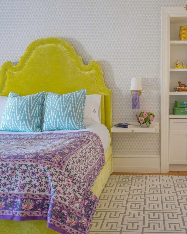 Bedroom with chartreuse headboard, blue chevron throw pillows and a purple floral bedspread.