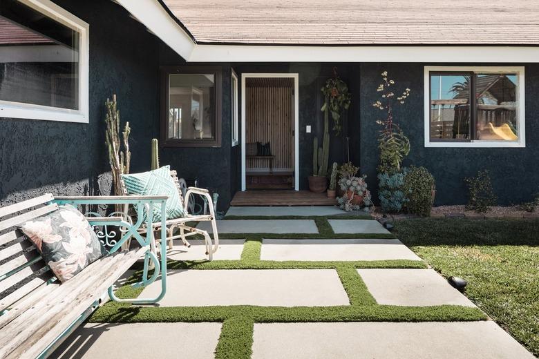 a yard with stone pavers with grass in between, plants are in a garden nearby