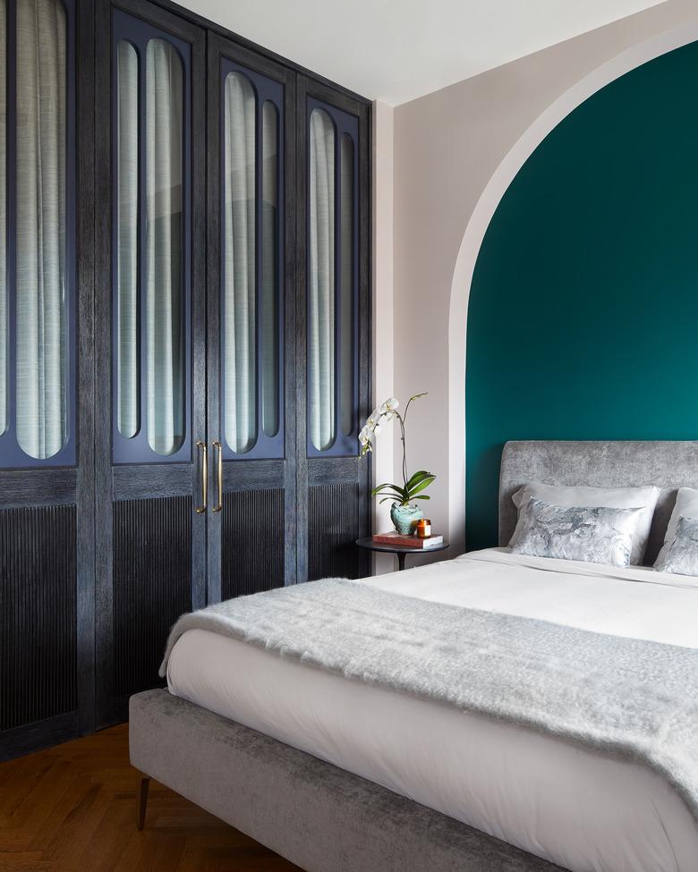 colorful bedroom with dark closet and green accent wall behind the bed