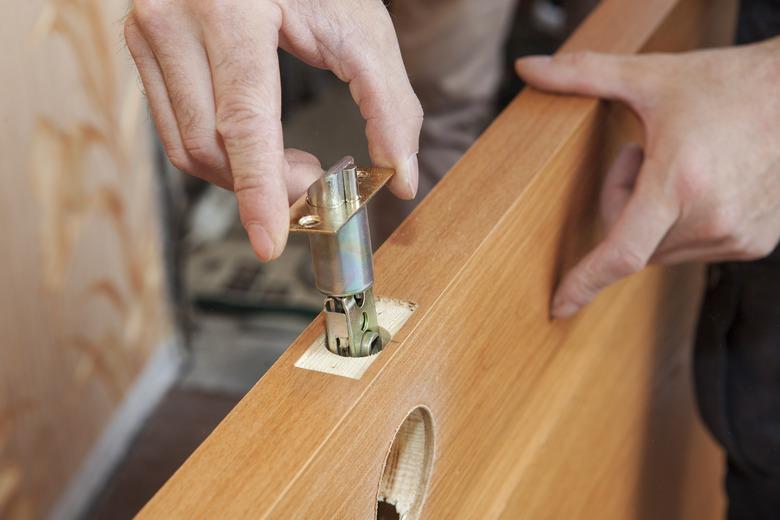 Close-up carpenter hands door lock installation.