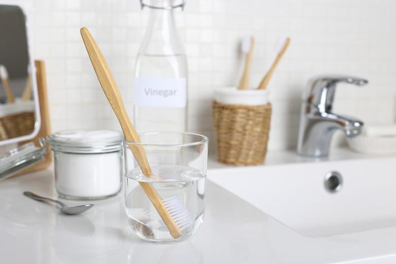 Cleaning a toothbrush with white vinegar, water and baking soda solution on the bathroom sink close up.