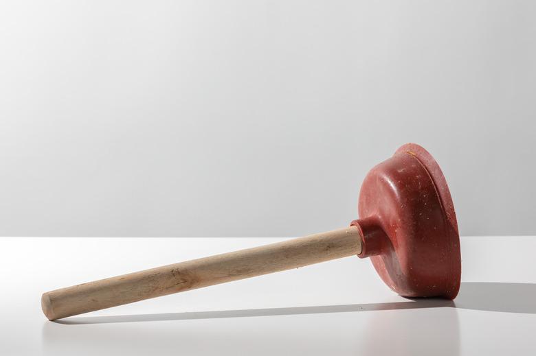 Old used red toilet plunger with wooden handle on a white background