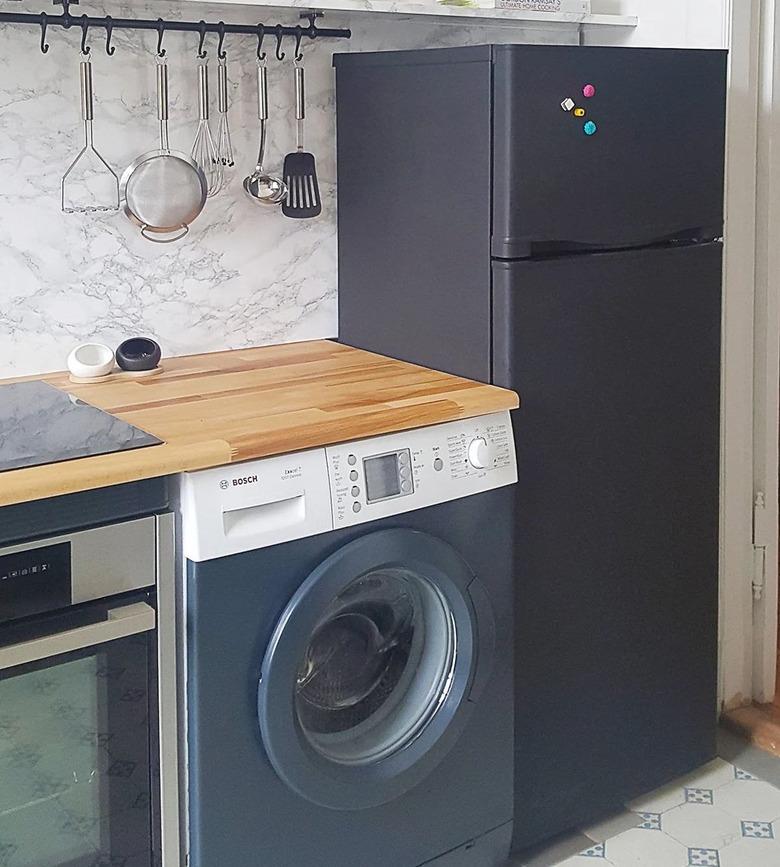 A painted black fridge next to a washing machine in a small kitchen